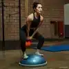 Kvinde balancerer på en BOSU-bold med en vægt.