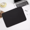 En sort 14" computersleeve ligger på et hvidt bord ved siden af en bærbar computer, en kop og airpods.