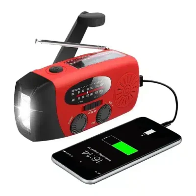 Rød nødradio med solcelle, håndsving, lommelygte og USB-port, der oplader en smartphone.