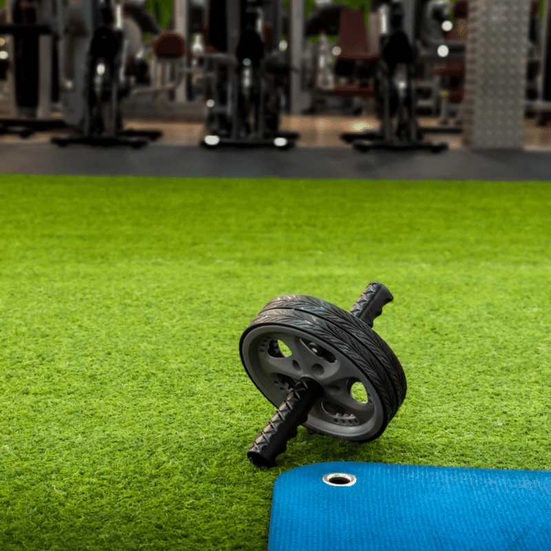 En ab wheel og træningsmåtte på et kunstgræsgulv i et fitnesscenter.