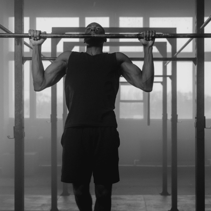 Mand iført sort tøj laver pull-ups på en stang.