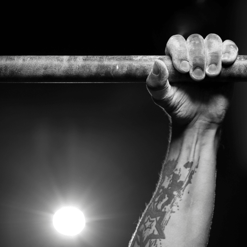Hånd grebet om en pull-up bar med en tatovering på underarmen.