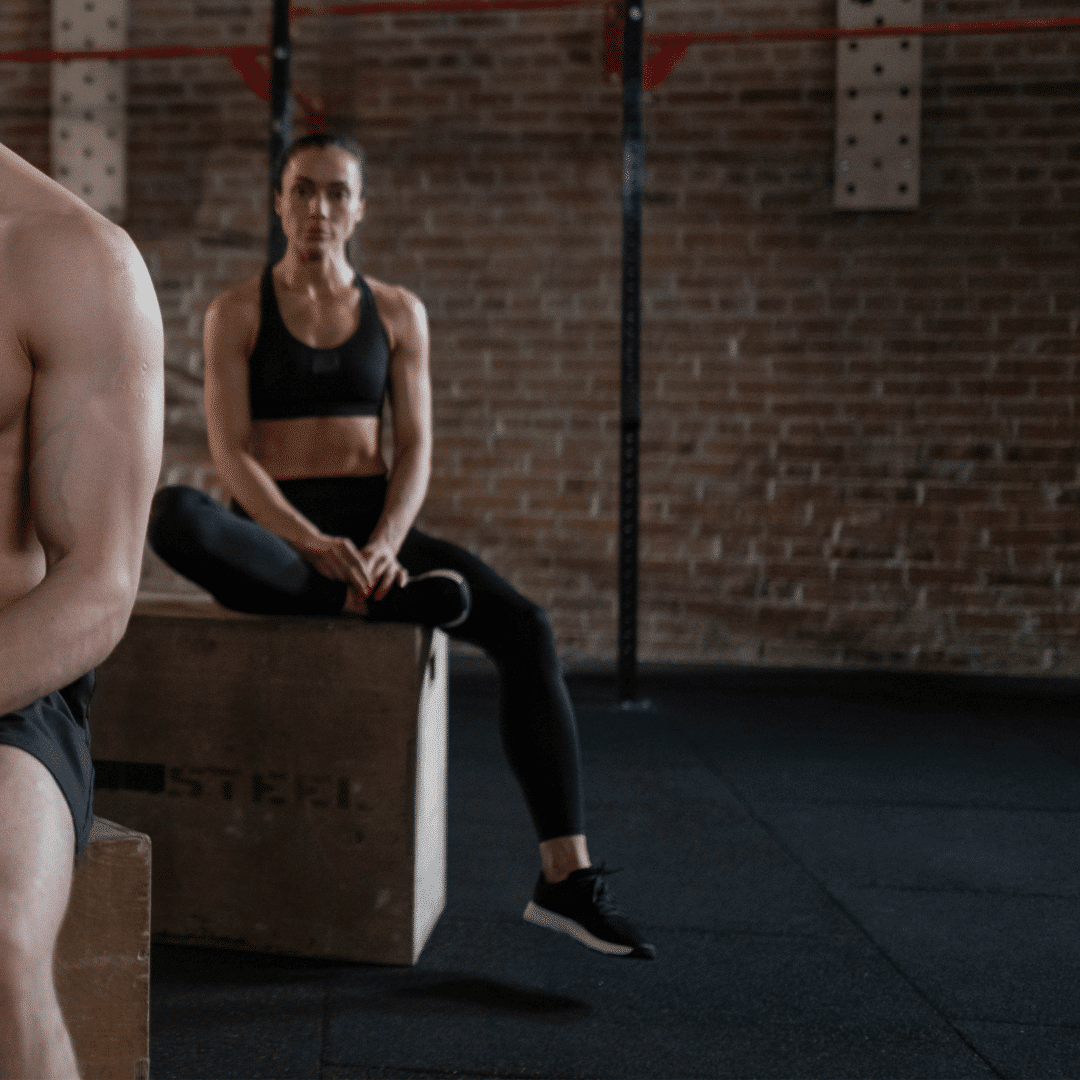 To personer i træningstøj sidder i et fitnesscenter.