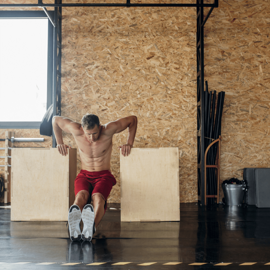 Mand laver tricep dips mellem to kasser i træningscenter.
