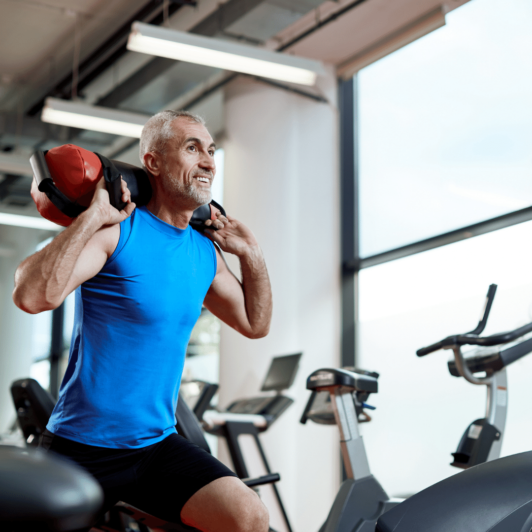 Ældre mand i blåt træningstøj løfter vægt i fitnesscenter.