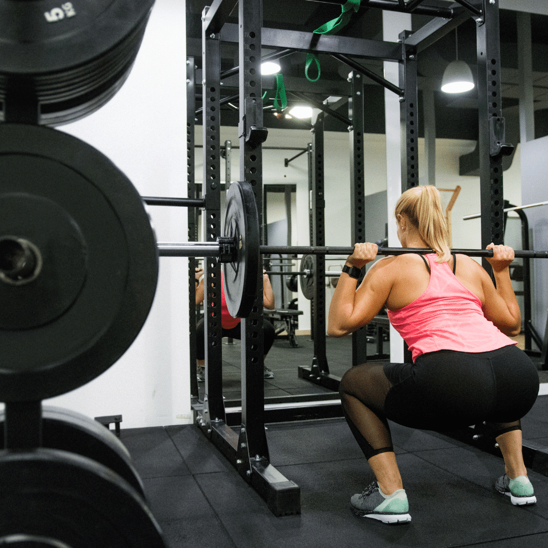 Kvinde laver squats med vægtstang i fitnesscenter.