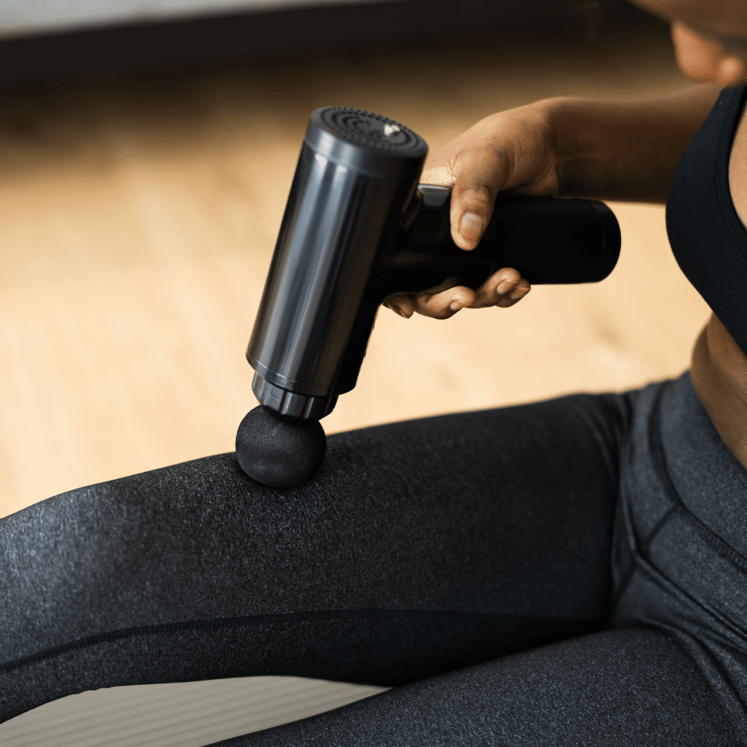 Person bruger en massagepistol på låret.