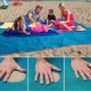 Familie sidder på et sandfrit tæppe på stranden.