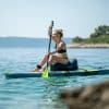 Kvinde sidder på et paddle board i klart hav.