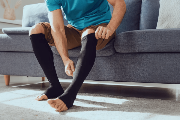 Støttestrømper. En mand sidder på en sofa og tager støttestrømper på.