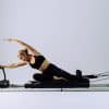 Kvinde i sort træningstøj træner på en Pilates-reformer