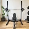 Træningsbænk og vægtstativ med vægtstænger i et fitnessrum.