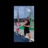 To personer løber langs en udendørs bane. Den ene person er iført en sort tanktop og shorts, mens den anden er klædt i hvidt og rødt sportstøj. Det ser ud til at være aften, da himlen er mørkere.