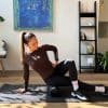 Kvinde træner med skumrulle på en yogamåtte indendørs.