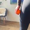 Hånd holder orange massagebold ved lår.