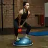 Kvinde balancerer på en bosubold med en kettlebell i et fitnesscenter.
