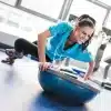 Kvinde udfører øvelse med BOSU-bold i fitnesscenter.