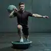 Mand træner med BOSU-bold og håndvægt.