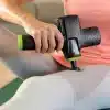 Person bruger en massagepistol på låret