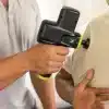 Person bruger en massagepistol på en andens skulder.