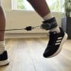 Person iført sort sneaker med fastgjort ankelrem og kabel.