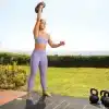 Kvinde iført træningstøj svinger en kettlebell udendørs.