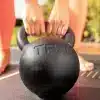 Hænder holder en TRX kettlebell udendørs.