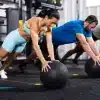 To personer udfører øvelser med medicinbolde i et fitnesscenter.