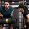 Mand træner med TRX-sandsæk under opsyn af kvindelig instruktør.