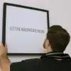 Person hænger en plakat op med teksten "Let the Adventure Begin".